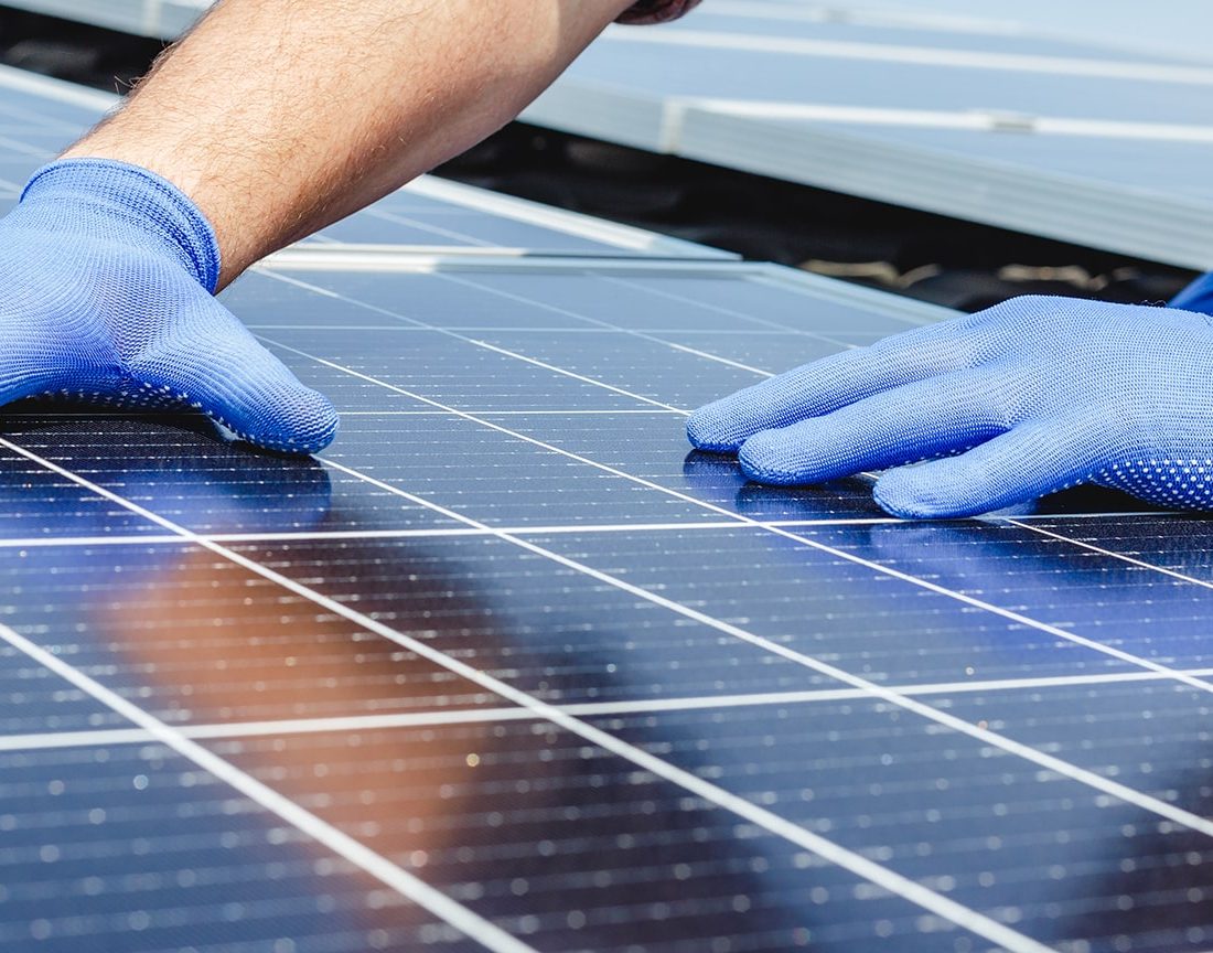 Photo d'un ouvrier posant un panneau solaire avec des gants bleus